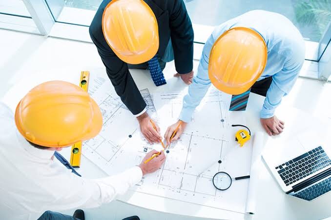 three-engineers-wearing-yellow-helmets-bent-over-a-drawing-in-analysis